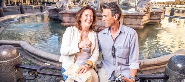 Paar im Alter von 50+ sitzt entspannt an einem Brunnen in Rom